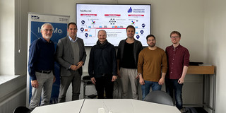 Professor Johannes Weyer, Christian Fronczak from MUNV, Marlon Phillipp, Kay Cepera, Antonio Isopp and Sebastian Hoffmann (from left to right) stand in front of a large monitor on which the main features of the Ne.Mobil project are shown..