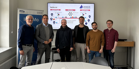 Professor Johannes Weyer, Christian Fronczak from MUNV, Marlon Phillipp, Kay Cepera, Antonio Isopp and Sebastian Hoffmann (from left to right) stand in front of a large monitor on which the main features of the Ne.Mobil project are shown..