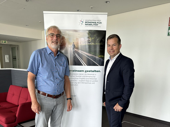 Johannes Weyer (TU Dortmund) and Jochen Harding (NRW.mobidrom) stand in front of a display by the Alliance for Mobility.