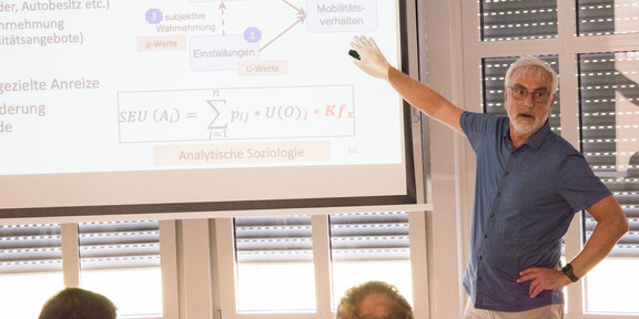 Prof. Weyer zeigt auf die Leinwand