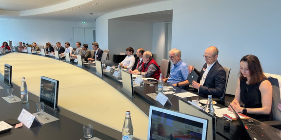 Around 20 people sit at an oval conference table.