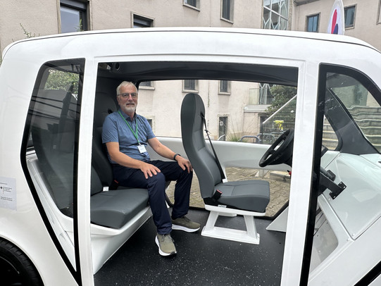 Johannes Weyer sitzt in dem weißen Cab auf der Rückbank. Das Cab ist zur Seite hin offen