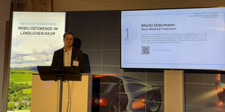 Moritz Ostermann steht hinter einem Rednerpult vor einem Banner auf dem "Mobilitätswende im ländlichen Raum" steht.
